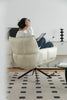 Lady sitting on a white armchair using a laptop in a modern living room.