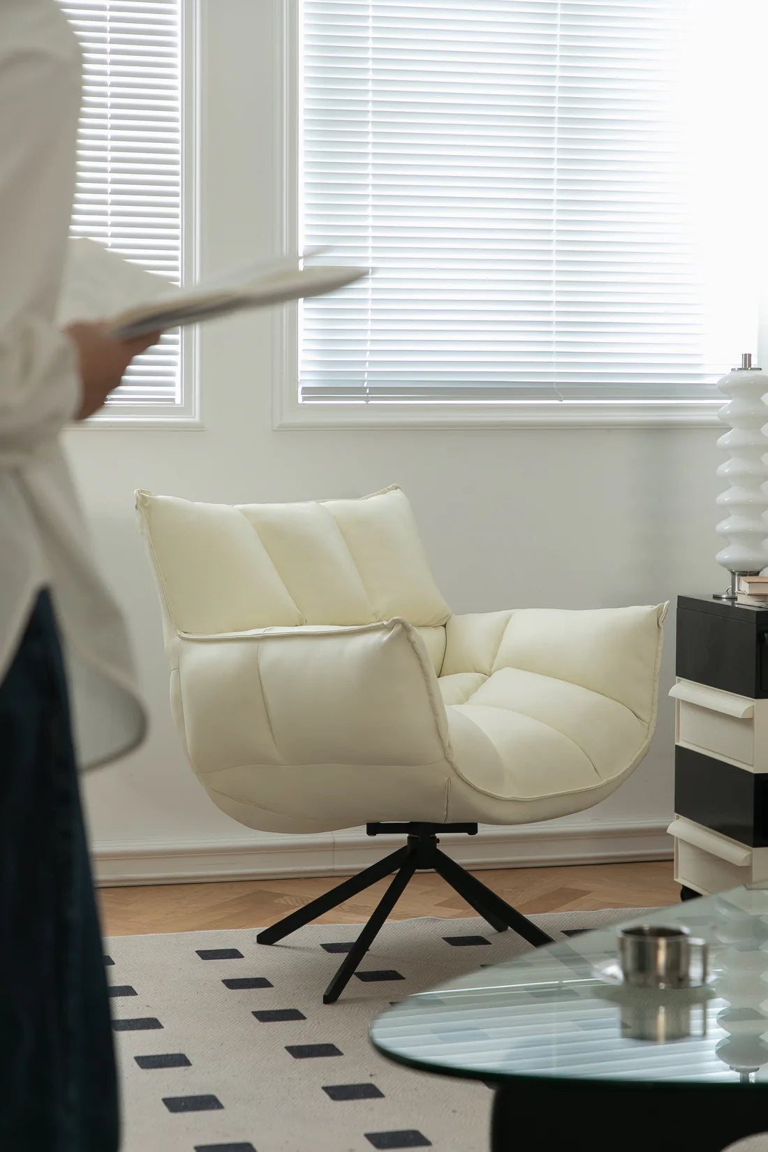 Modern living room with a white swivel armchair, glass coffee table, and decorative items.