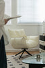 Modern living room with a white swivel armchair, glass coffee table, and decorative items.