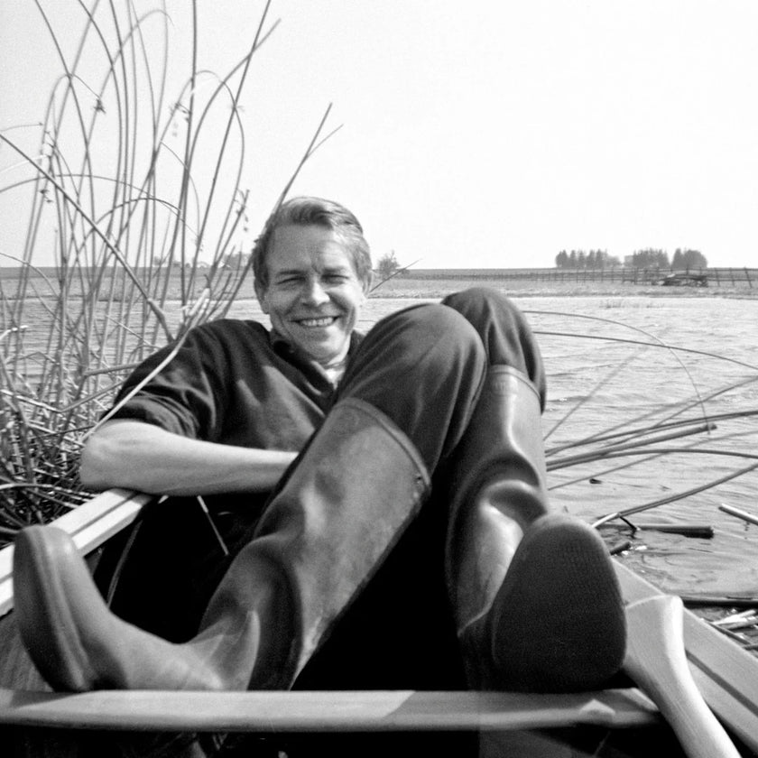 Man sitting in a boat by a lake with reeds in the background