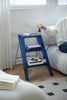 Blue step ladder shelf with books and a bottle on a wooden floor next to a white couch.
