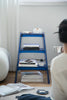 Lady sitting on a couch looking at a blue step ladder display shelf with books and a box on it.