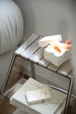 Small metal storage shelf with books and a white box on a neutral background