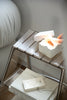 Small metal storage shelf with books and a white box on a neutral background