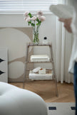 Decorative three-tiered ladder shelf with books and a vase of flowers in a room setting.