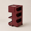 A dark red plastic rolling organizer cart with multiple drawers, shelves, and open compartments, shown on a plain beige background.