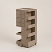 A modern, minimalist rolling storage organizer in a brown color, featuring a stack of drawers on the left, open shelves with curved cutouts on the right, and a top tray, all mounted on small caster wheels.