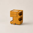 A ginger yellow ABS plastic storage cart with two drawers, open shelving, and small wheels, shown on a clean, light beige background.