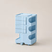 A light blue rolling storage organizer with four drawers on the left and three open shelves on the right, set against a solid beige background.
