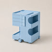 A light blue ABS plastic rolling storage cart with three drawers on the left, two open shelves with curved cutouts on the right, and small caster wheels at the base, shown on a plain beige background.