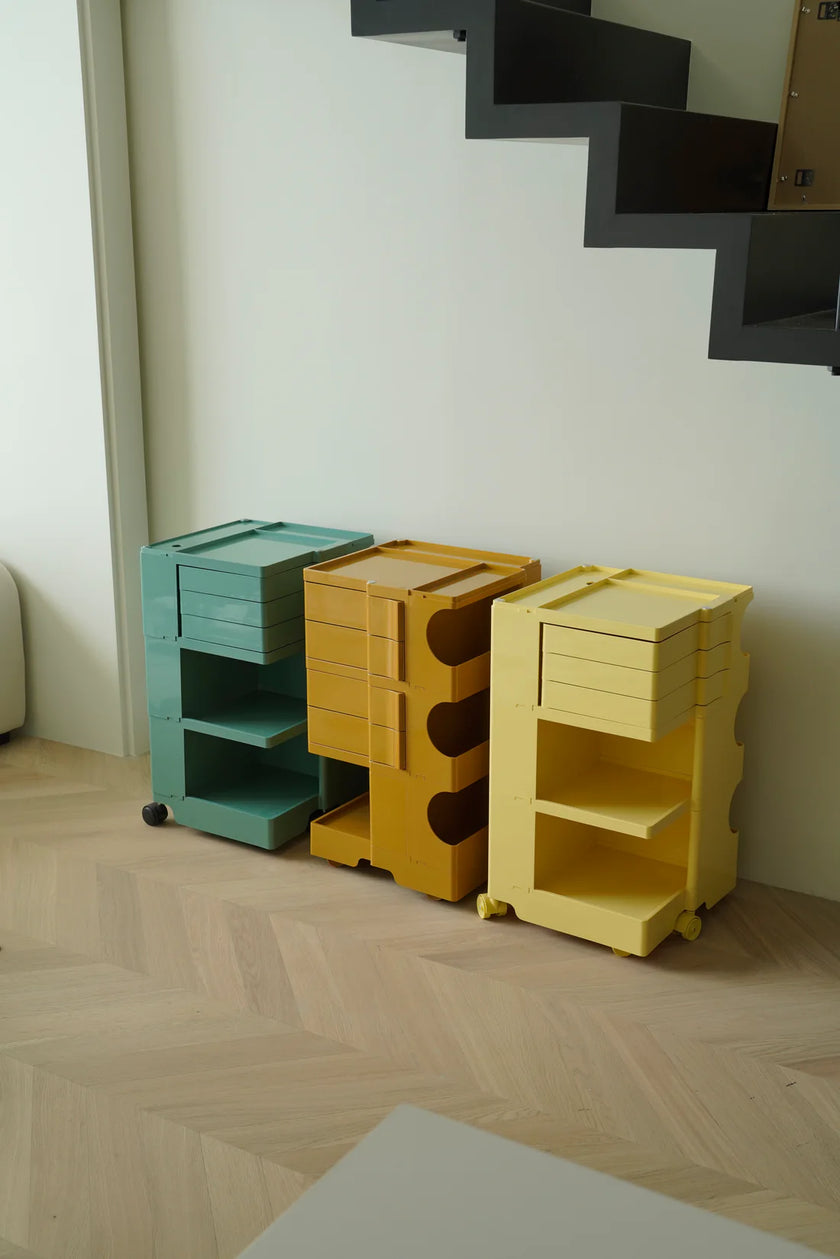 Three colorful storage units against a white wall with a staircase.
