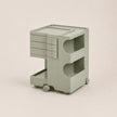 A light matcha green ABS plastic rolling storage cart with three drawers on the left, open shelves on the right, and caster wheels at the base, shown on a solid light beige background.