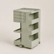 A light sage green plastic rolling organizer cart with a top drawer unit, three open shelves, and caster wheels, shown against a solid light beige background.