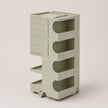 A light sage green storage cart with five tiers, featuring a stack of drawers on the upper left and open arch-shaped shelves on the right, set against a solid light beige background.