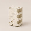 A cream-colored plastic rolling storage organizer with four drawers on the left and three open shelves on the right, set against a solid light beige background.