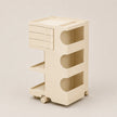 A cream-colored plastic rolling storage cart with three drawers, three open shelves, and wheels, shown on a neutral beige background.