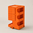 Bright orange ABS storage cart with multiple drawers and open shelves on wheels, photographed on a clean light beige studio background.