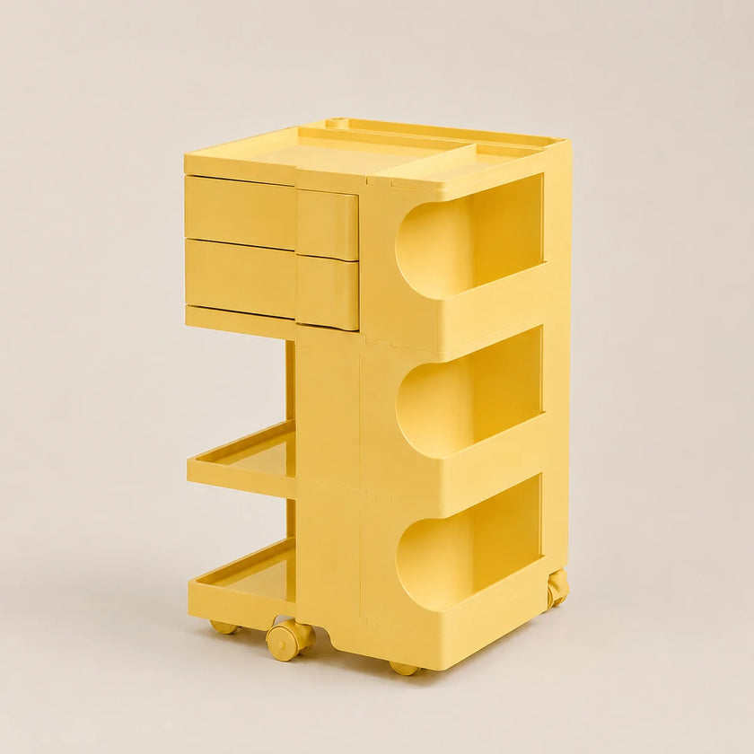 A bright yellow rolling storage cart with two drawers on the left, open shelves in the middle, and a top platform, shown on a plain light beige studio background.