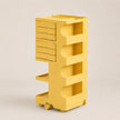 A bright yellow rolling storage organizer with six drawers on the left, four open shelves on the right, and small caster wheels at the base, photographed on a clean light gray studio background.