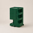A dark green rolling storage cart with multiple drawers and open shelves, photographed on a plain light beige studio background.