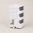 A white ABS rolling storage organizer with five drawers on the left and three open shelves on the right, set against a solid light beige background.