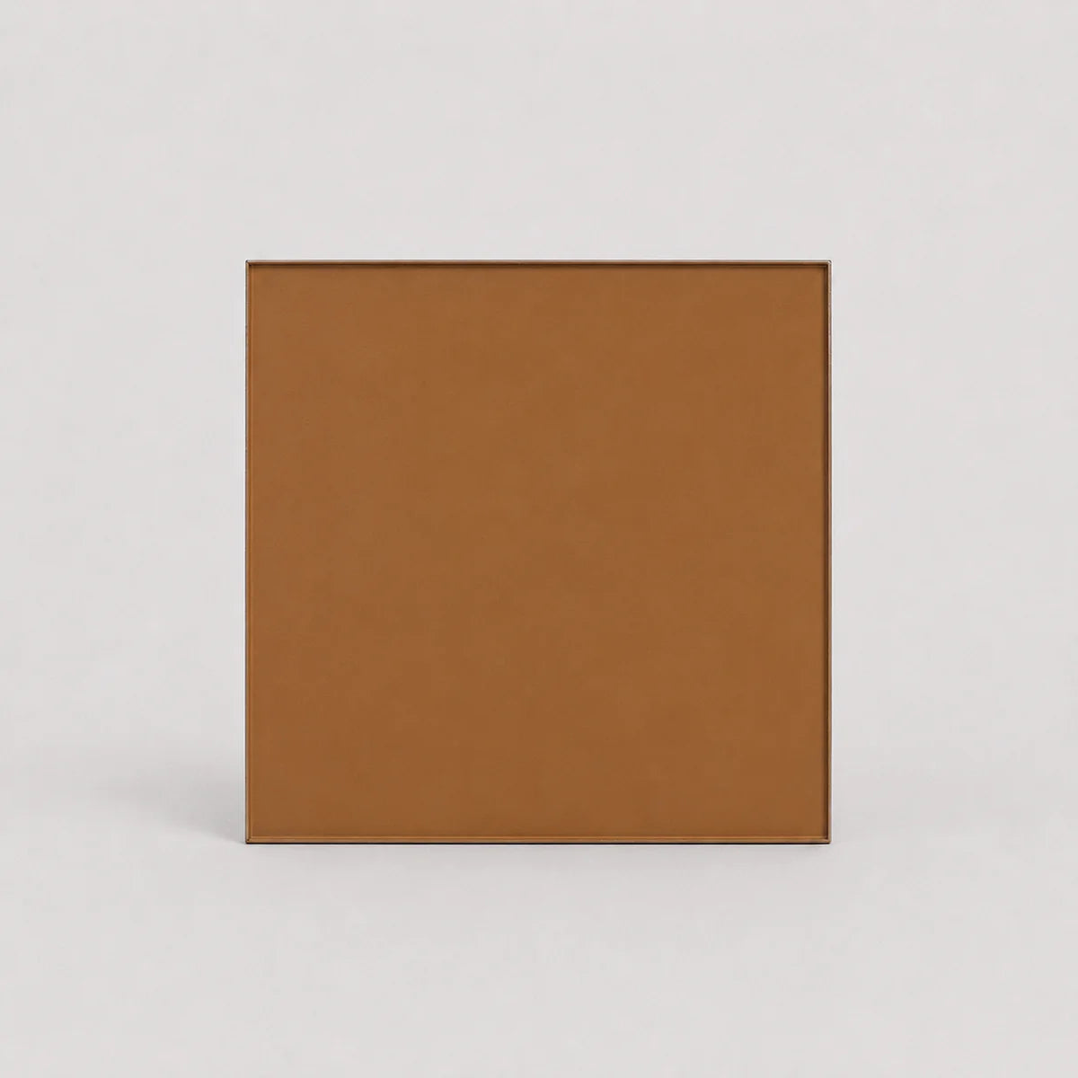 A square tan-brown textured panel or tile with a thin dark border, centered on a light gray background.