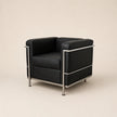 A mid-century modern armchair with black leather upholstery and a polished chrome steel frame, shown against a solid warm beige background.