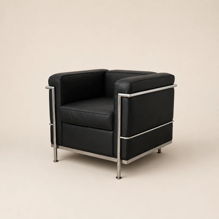 A mid-century modern armchair with black leather upholstery and a polished chrome steel frame, shown against a solid warm beige background.
