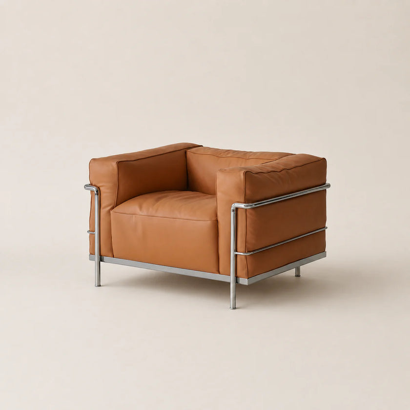 A modern leather armchair with a warm camel-brown seat and back cushions, supported by a slim polished steel frame with legs, photographed against a solid light beige background.