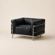 A mid-century modern armchair with black leather upholstery and a polished steel frame, photographed against a solid light beige background.