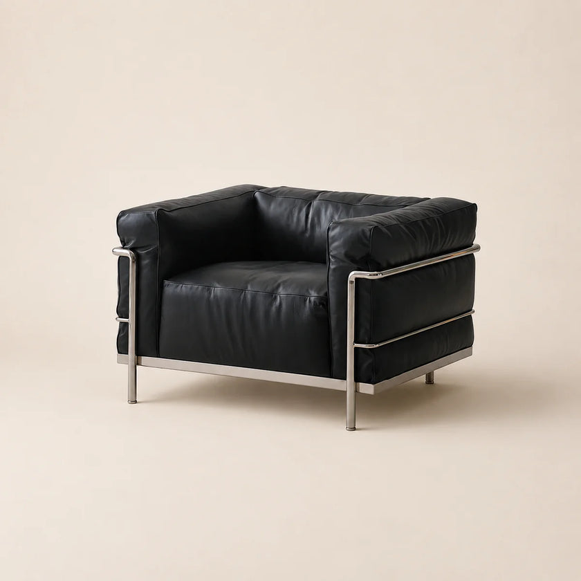 A mid-century modern armchair with black leather upholstery and a polished steel frame, photographed against a solid light beige background.