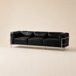 A modern three-seat sofa with black leather cushions and a polished chrome metal frame, set against a solid beige background.