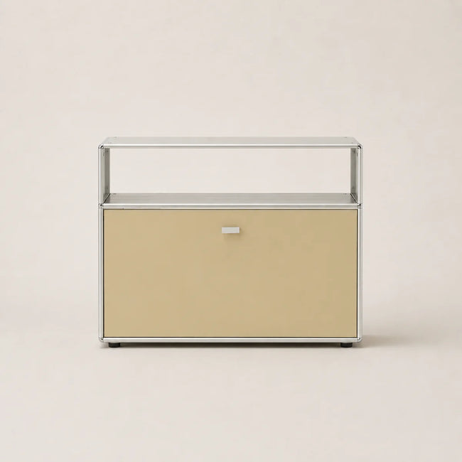 A modern modular two-tier storage cabinet with a warm beige lower drawer and a clear glass upper shelf, framed in polished silver-toned metal, set against a solid light beige background.