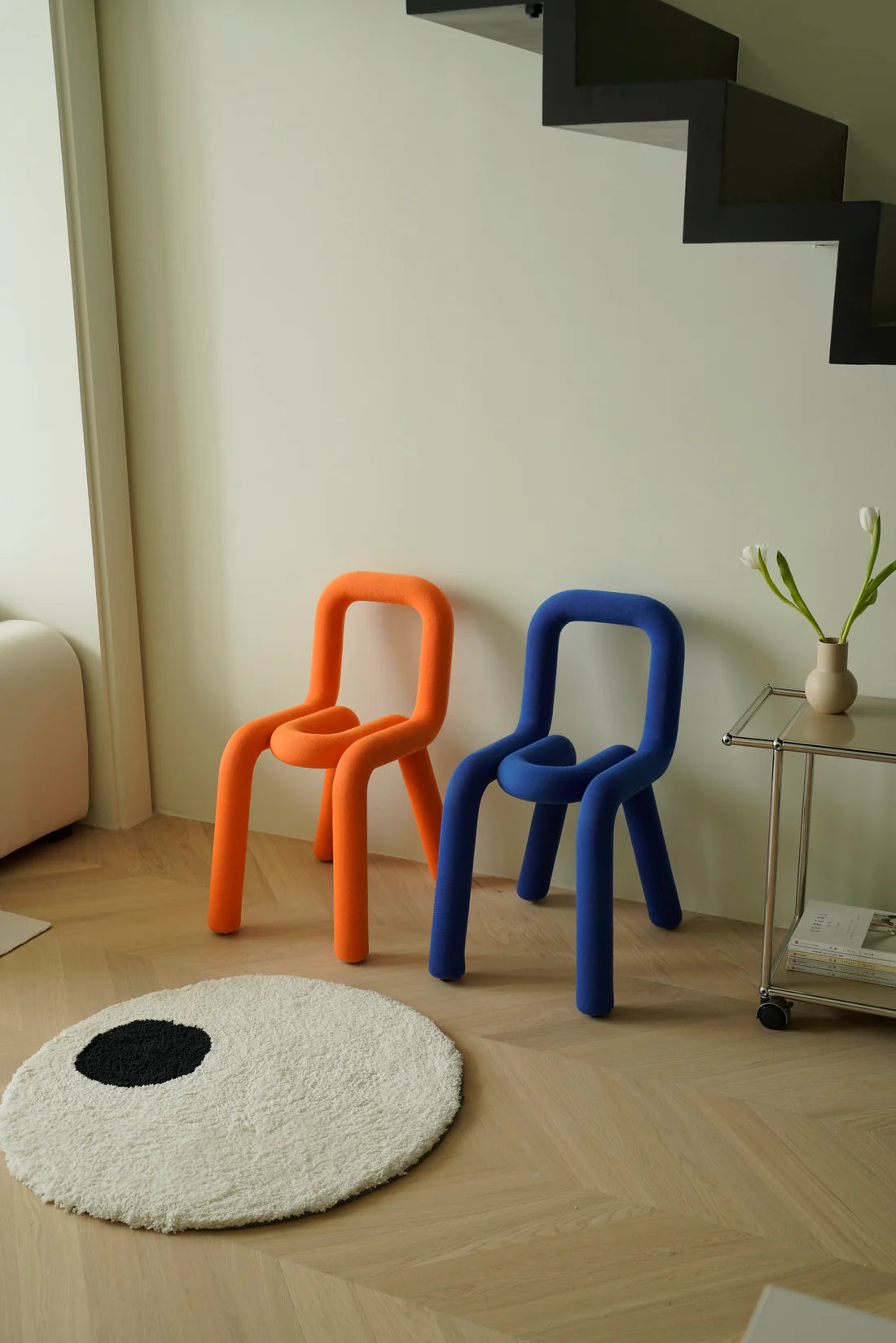 Two colorful kids chairs, one orange and one blue, in a room with a white rug and a small table with plants.
