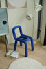 Blue vanity chair in a room with a lamp, books, and a painting on a light-colored floor.