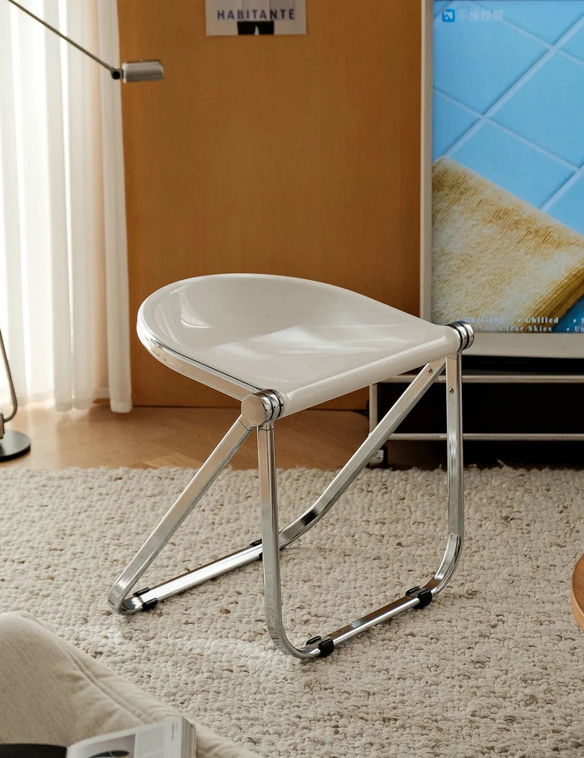 A modern white molded seat stool with a chrome metal frame, shown in a cozy living room setting on a textured beige rug.