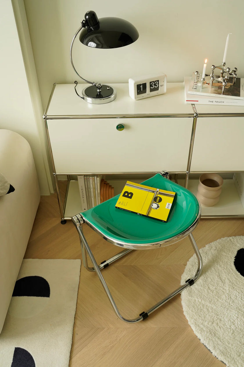 Green stool with a yellow book on a wooden floor next to a white cabinet.
