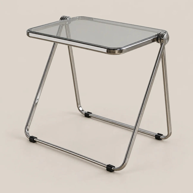 A modern folding side table with a clear glass top and a chrome metal frame, shown on a solid light beige background.