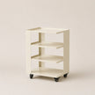 Beige bookshelf with three shelves on wheels against a beige background