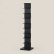 A tall, narrow black metal storage rack with multiple small shelves, shown against a plain warm beige background.