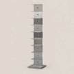 A tall, narrow modern shelf made of brushed silver metal, featuring multiple stacked rectangular compartments, set against a solid light beige background.