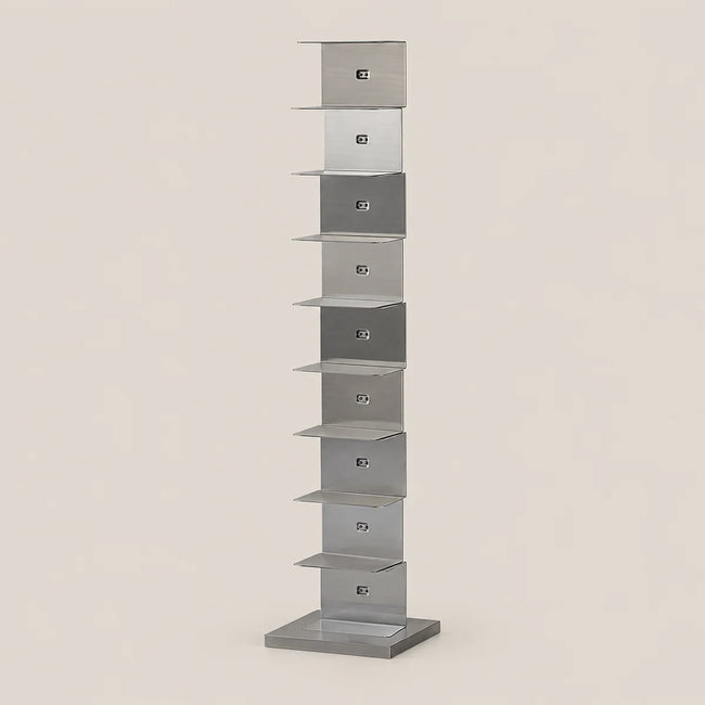 A tall, narrow modern shelf made of brushed silver metal, featuring multiple stacked rectangular compartments, set against a solid light beige background.