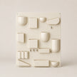 White wall-mounted shelving unit with various geometrically shaped shelves on a light beige background