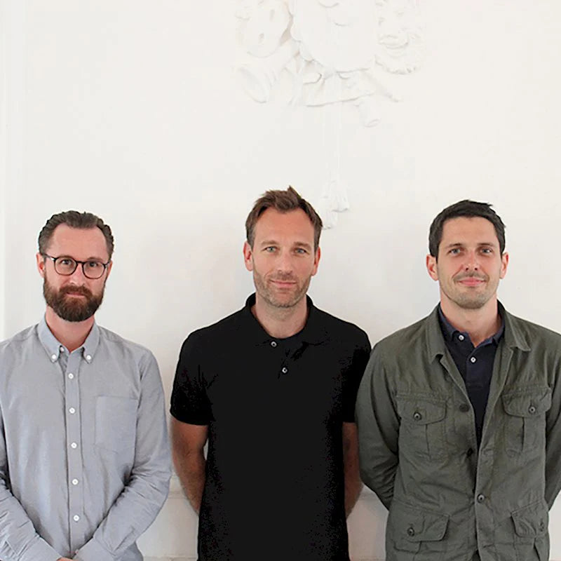 Three men standing side by side against a white wall.