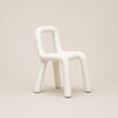 A minimalist white molded chair with a rounded, organic silhouette and thick legs, set against a solid warm beige background.