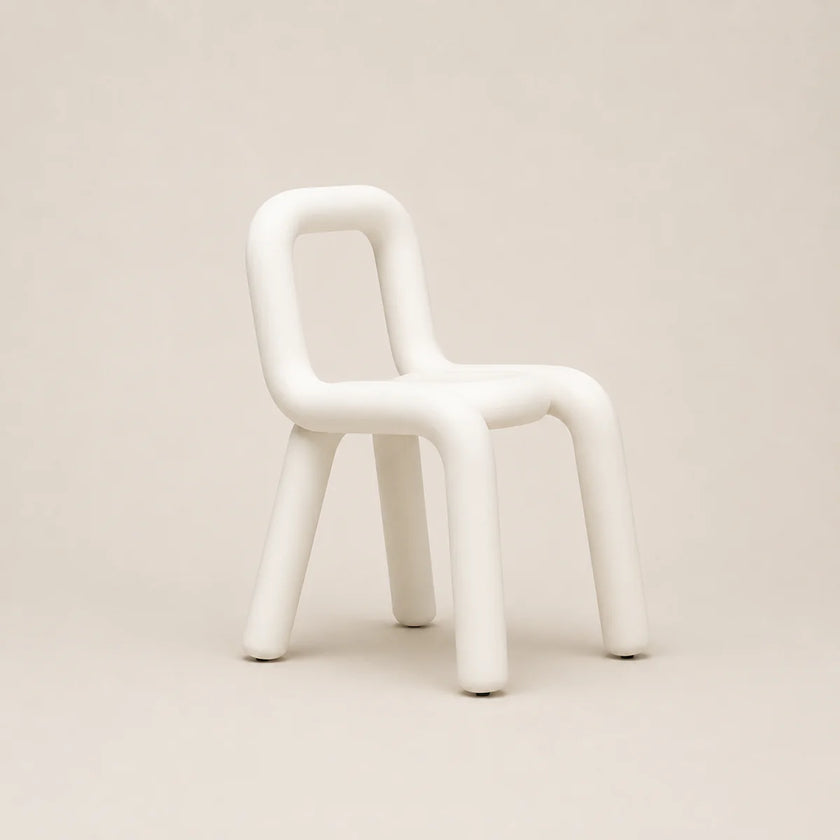 A minimalist white molded chair with a rounded, organic silhouette and thick legs, set against a solid warm beige background.