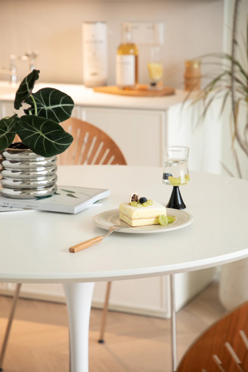 Small cake on a plate with a fork on a white round dining table, plant and candle in the background