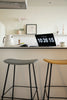 Two bar stools in a kitchen setting with a laptop displaying numbers on a white countertop.