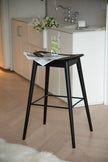 Black bar stool with a newspaper on a wooden floor in a kitchen setting.