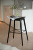 Black bar stool with a newspaper on a wooden floor in a kitchen setting.
